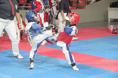 A young taekwondo jin in red armor connects with a decisive head kick during a sparring match in the previous SMART/MVPSF Summer Clinic.