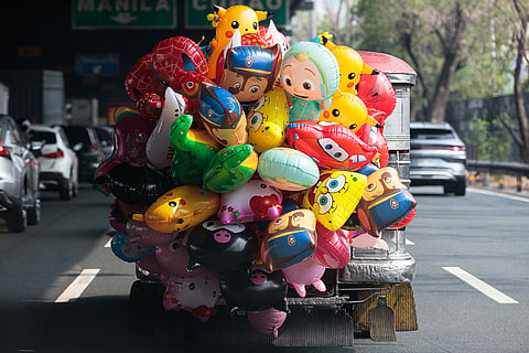 A vendor selling cartoon-shaped party balloons sits on the stepboard of a jeepney as it cruises along the South Luzon Expressway (SLEX) northbound in Makati City on Saturday, 16 May 2026.
