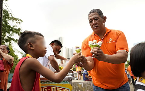 A VOLUNTEER from Solaire Cares gives ice cream to a young Quezon City resident during the charity organization’s Balik-Eswela outreach program that saw employees of Solaire Resort North distribute school bags and supplies to hundreds of grade-schoolers from Barangay Bagong Pag-Asa ahead of the reopening of classes in June. 