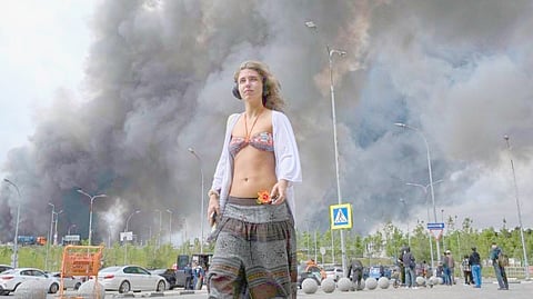 A WOMAN walks outside a shopping mall as black smoke rises from the area of the Russian oil producer Gazprom Neft’s Moscow oil refinery on the south-eastern outskirts of Moscow on 18 June 2026.