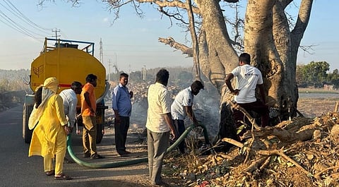 ಆನೇಕಲ್​ ತಾಲೂಕಿನ ಹುಲಿಮಂಗಲ ರಸ್ತೆಯ ಕೆರೆ ಏರಿ ಮೇಲೆ ಬೆಳೆದು ನಿಂತಿದ್ದ ನೂರಾರು ವರ್ಷಗಳ ಮರಕ್ಕೆ ಬಿದ್ದ ಬೆಂಕಿ ನಂದಿಸುವ ಕಾರ್ಯದಲ್ಲಿ ತೊಡಗಿರುವ ಜಿಗಣಿ ಪುರಸಭೆ ಸಿಬ್ಬಂದಿ. 