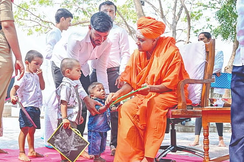ಮಗುವಿನ ಕೈಯಿಡಿದು ಅಕ್ಷರ ಬರೆಸುತ್ತಿರುವ ಗವಿಶ್ರೀಗಳು.