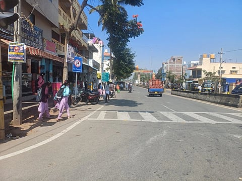 ಚಾಮರಾಜನಗರದ ಸಂತೇಮರಹಳ್ಳಿ ವೃತ್ತದಲ್ಲಿ ತಂಗುದಾಣವಿಲ್ಲದೇ ಅಂಗಡಿ ಮುಂಗಟ್ಟುಗಳ ಮುಂದೆ ಪ್ರಯಾಣಿಕರು ಕಾಯುತ್ತಿರುವುದು 