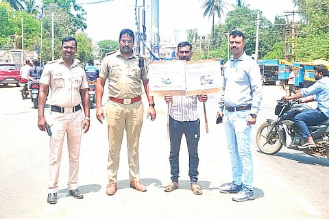  ಕಡೂರಲ್ಲಿ ಸಂಚಾರಿ ನಿಯಮ ಉಲ್ಲಂಸಿದ ವ್ಯಕ್ತಿ ಮರವಂಜಿ ಸರ್ಕಲ್ ಬಳಿ ಕಮ್ಯುನಿಟಿ ಸೇವೆ ಮಾಡುವಂತೆ ಟ್ರಾಫಿಕ್ ರೂಲ್ಸ್ ಇರುವ ಬೋರ್ಡ್ ಅನ್ನು ಹಿಡಿದುಕೊಂಡು ನಿಂತಿರುವುದು.