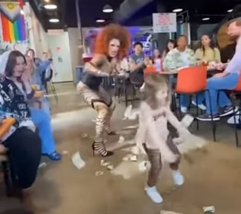 A drag queen performer showers a child with cash. Location unknown. 