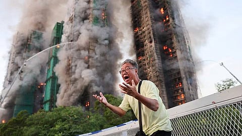 An individual standing outside of the Wang Fuk Court housing complex in Hong Kong as the complex's fire continues to burn.  